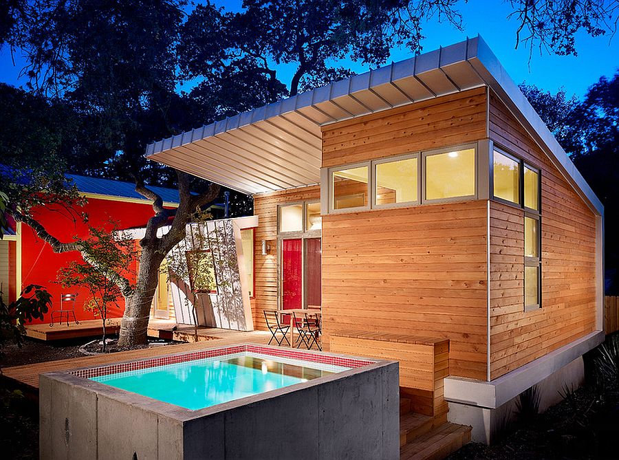 A concrete modern small pool in the front of a tiny yet modern wood home.