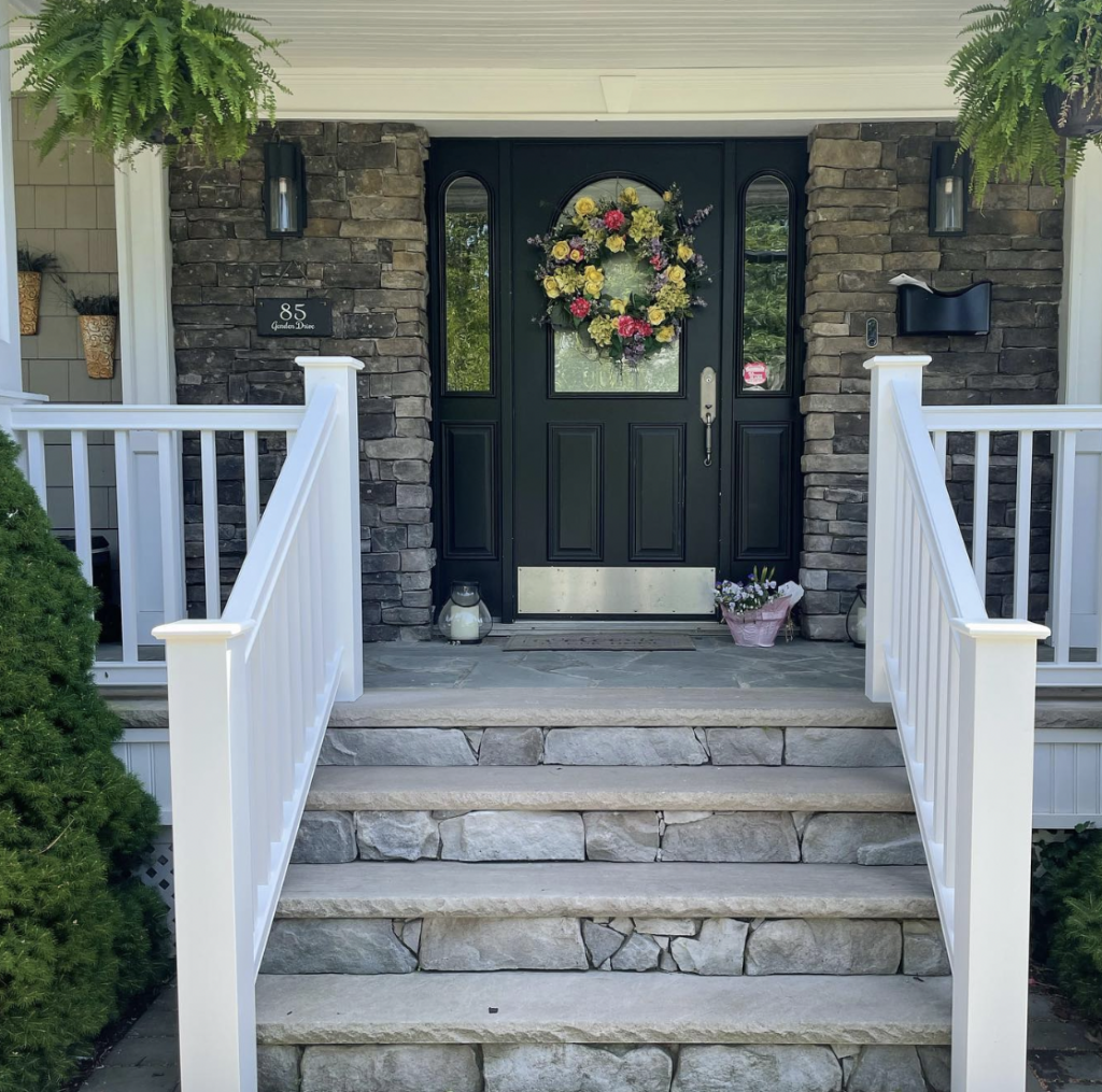 A farmhouse porch with a black door and railing