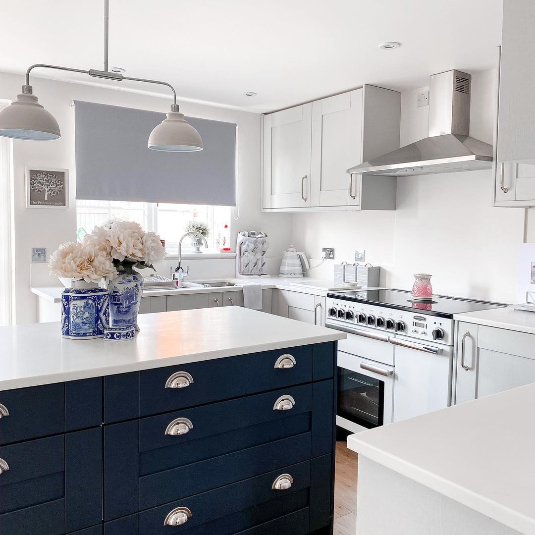 Navy island with white countertops, silver hardware, and utilitarian pendants