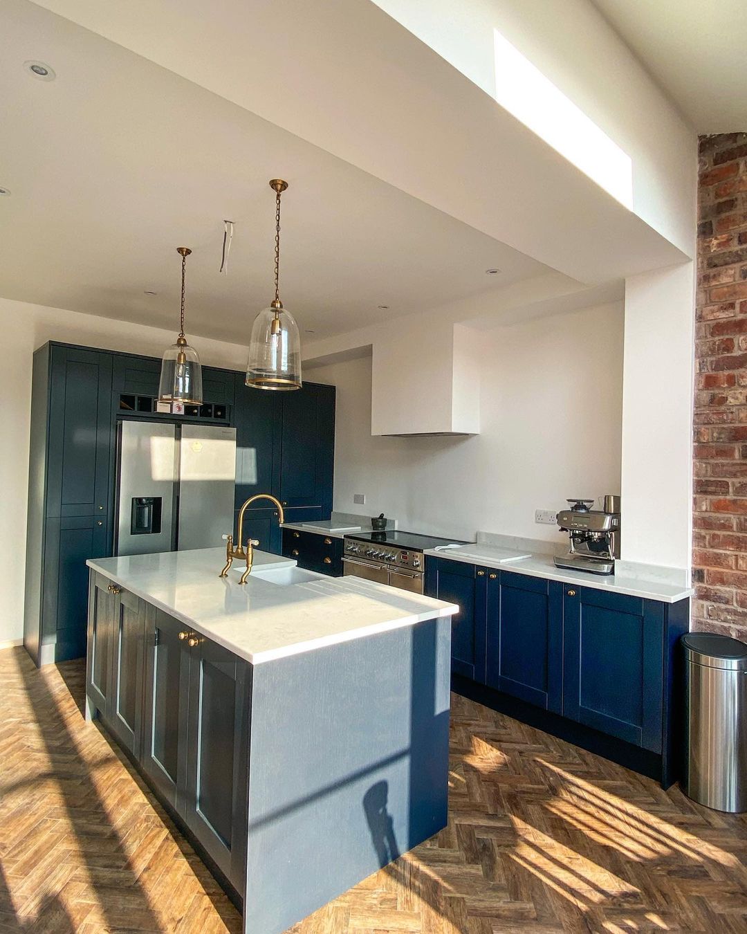 Navy island kitchen with brick accent wall, herringbone flooring, and gold fixtures