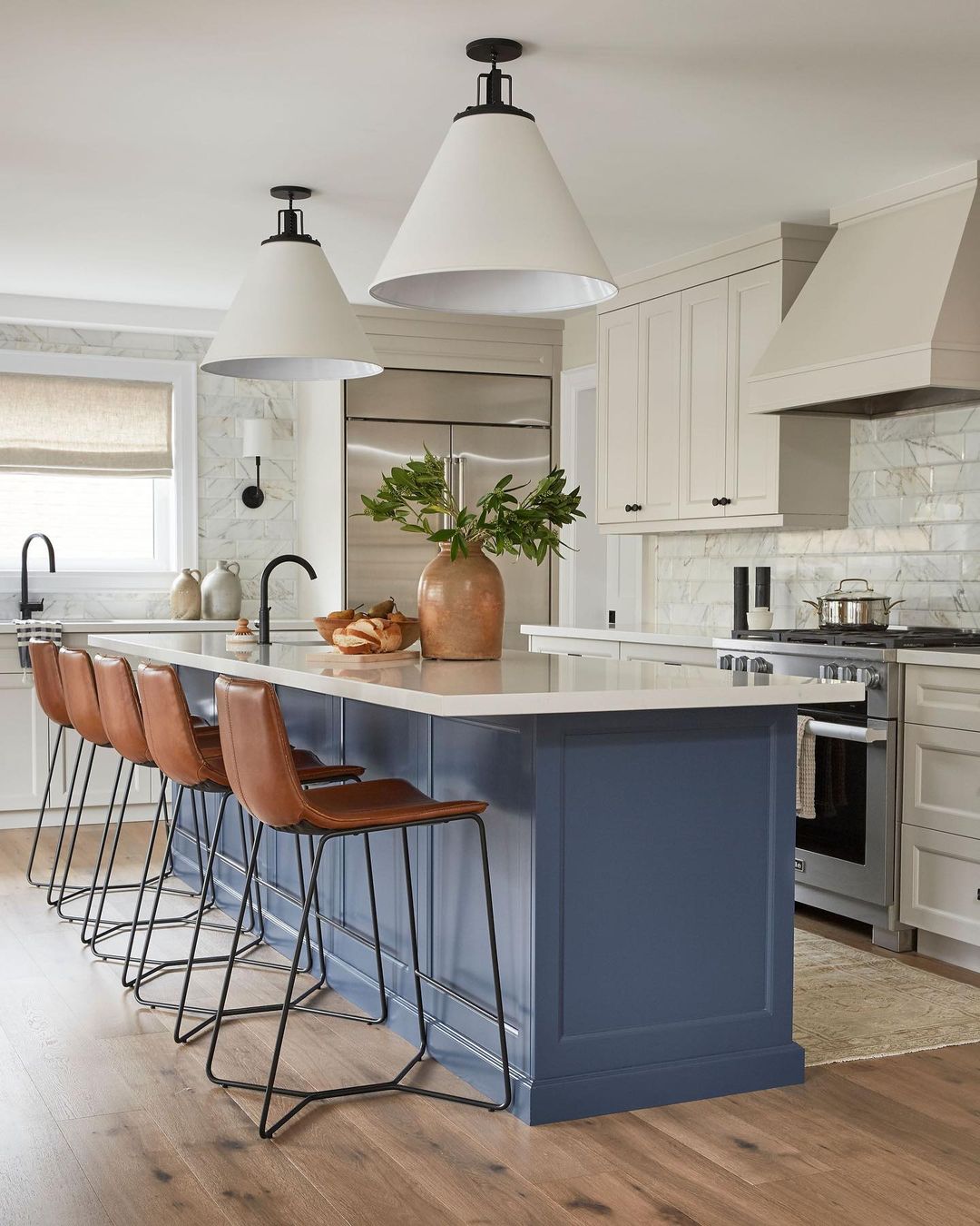 Navy island with leather stools and large pendant lights in a neutral kitchen