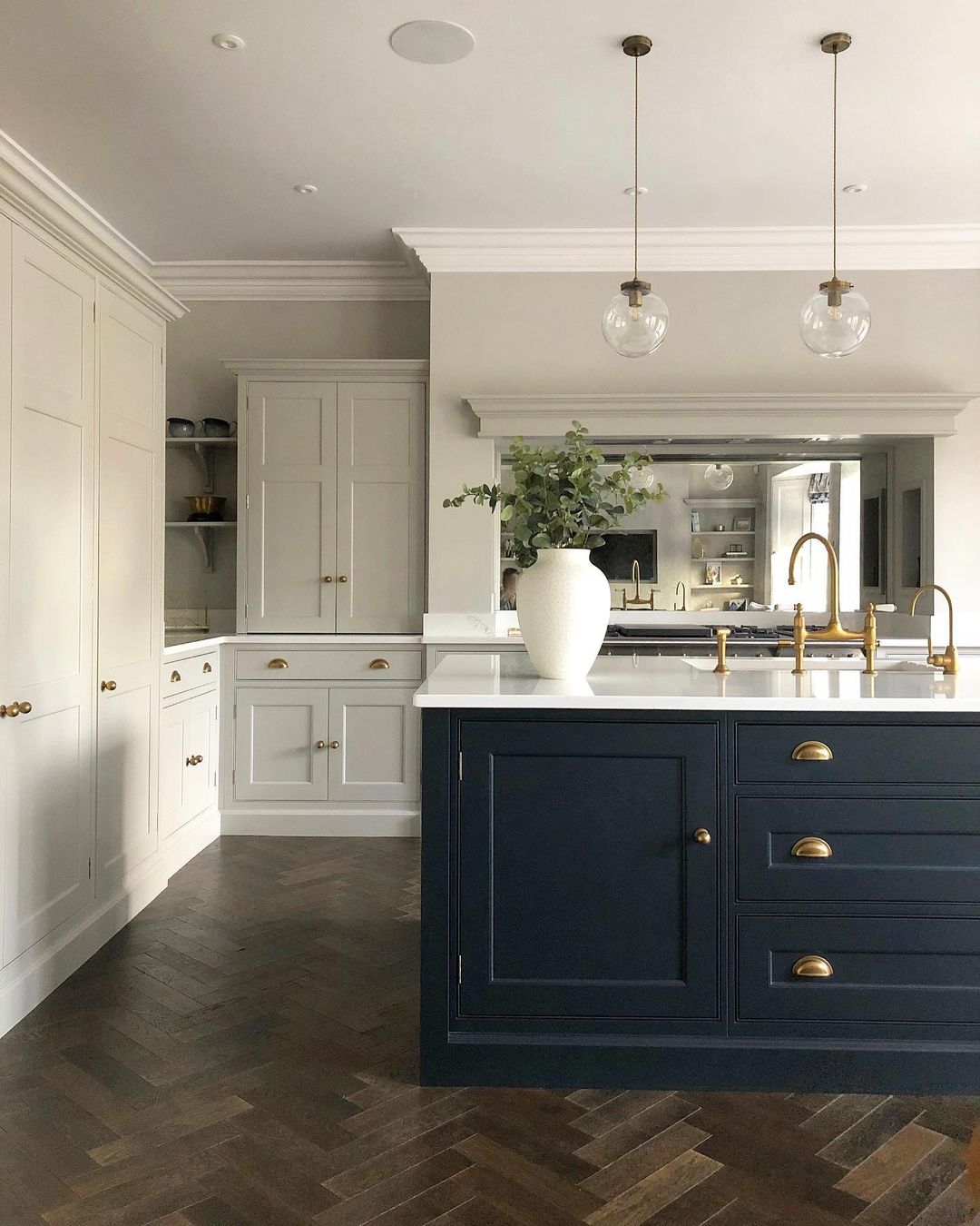 Navy island in open-plan kitchen with herringbone wood floors and glass pendants