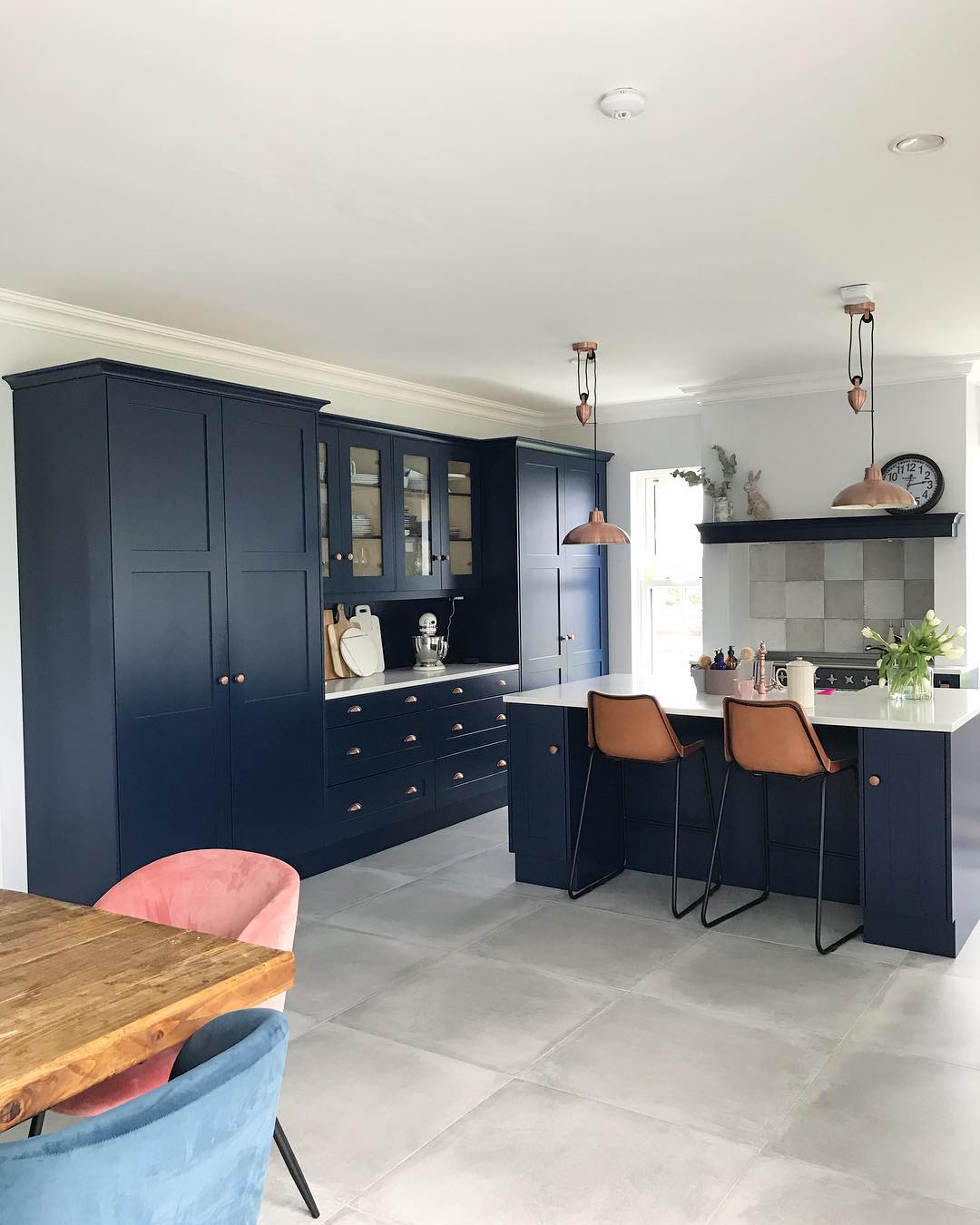 Navy island with copper pendant lights and leather stools