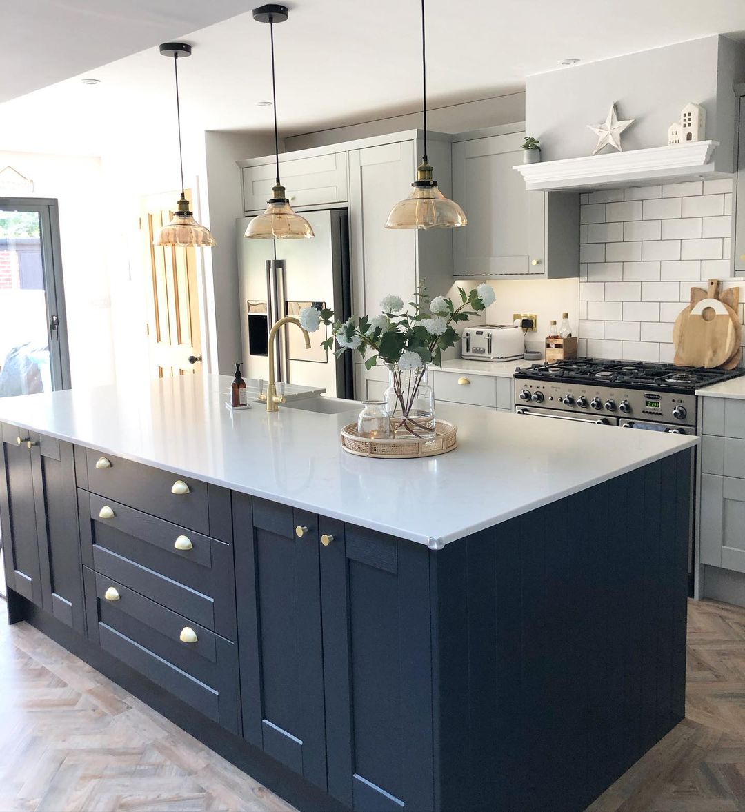 Navy cabinetry island with gold handles, glass pendants, and white countertop