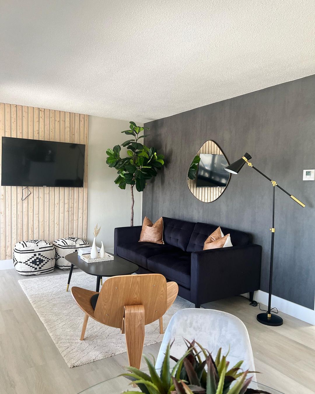 Round mirror beside a black couch and wood panelling